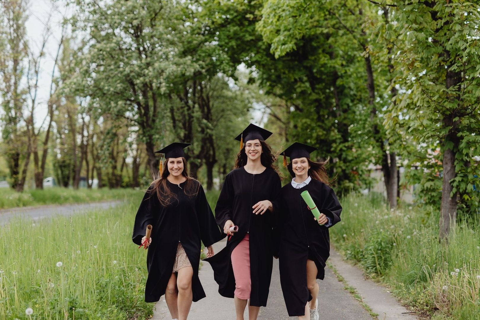 Tre nyutexaminerade studenter går på en grönskande gångväg